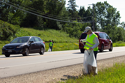 A member of the Ozaukee County Corvette Club wearing a fluorescent yellow safety vest cleans up garbage along WIS 60.