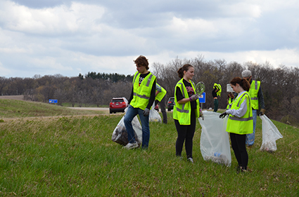 Edgewood college students wearing fluorescent yellow safety vests clean up garbage along U.S. 18.