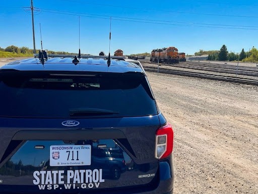 Wisconsin State Patrol cruiser with red lights on near a railroad