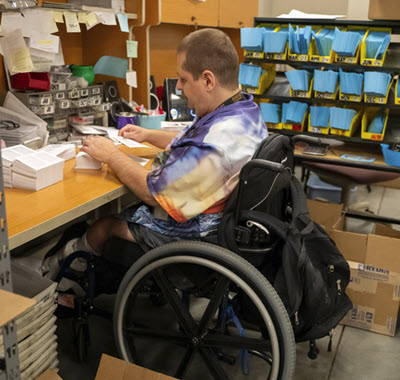 Man in wheelchair processing license plates in envelopes