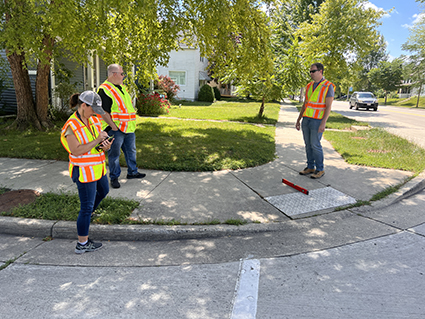 Three WisDOT staff in yellow and orange safety vests evaluate a curb ramp for improvements.