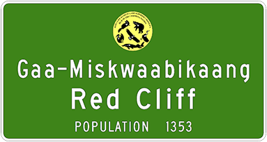 Green road sign that says Gaa-Miskwaabikaang, Red Cliff, and population 1353. 