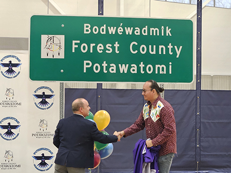 A WisDOT representative and a member of Forest County Potawatomi shake hands at the dual-language sign unveiling.