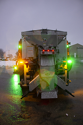 The rear view of a snow plow outfitted with flashing green lights.