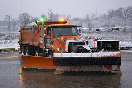 An orange snow plow with flashing green and amber lights.