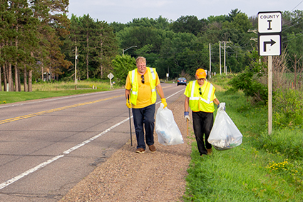 Two volunteers wearing safety vests work along WIS 53.