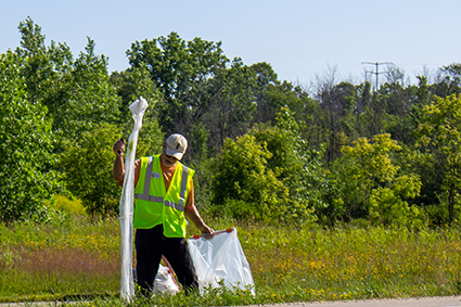 Volunteer wearing a safety vest cleans up a large piece of plastic.
