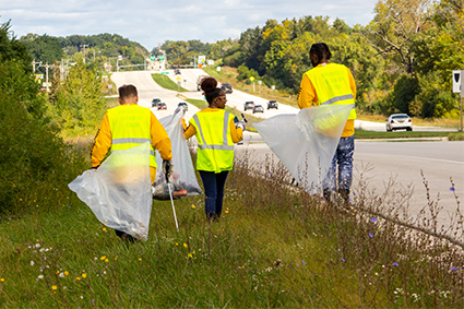 Three volunteers wearing yellow safety vests walking along  Highway 164.