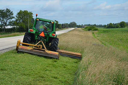 A tractor pulling a mower mows alongside a state highway.