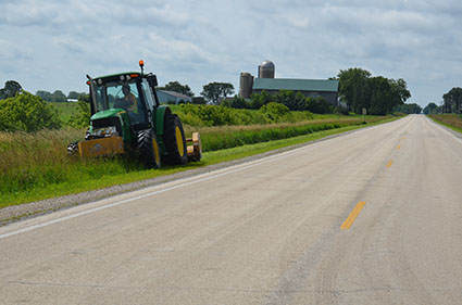 A tractor mows a roadside in a rural area.