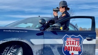 A female Wisconsin State Patrol trooper conducting speed enforcment with a laser, standing outside a Dodge charger in a winter