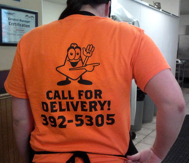 The back of an orange t-shirt, with a illustration of a construction cone and the words  "Call For Delivery! 392-5305"