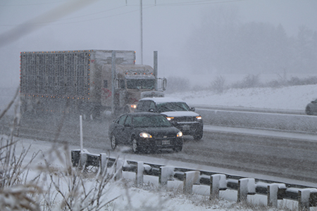 A car, SUV and semi-truck driving in very snowy conditons.