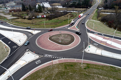 An aerial view of a roundabout .  Several cars and trucks are driving on the roundabout.